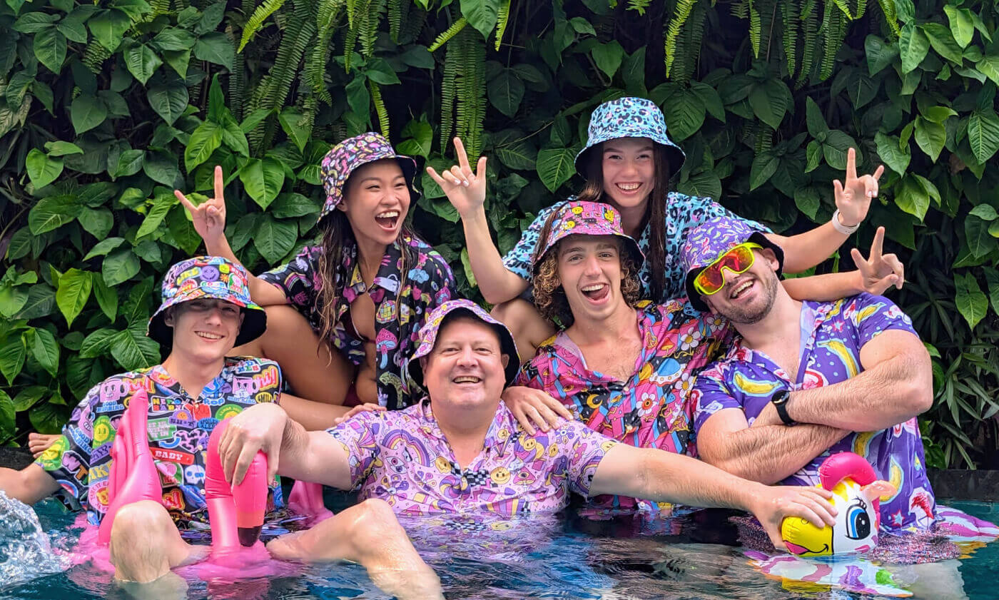Group of people in bad shirts and matching funny bucket hats posing by a pool.