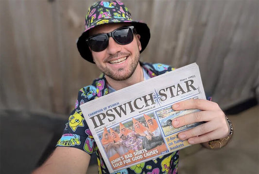 Shit Shirt Club founder, John Parnell, holds front page of newspaper which reads "Johns bad shirts sold for good causes"