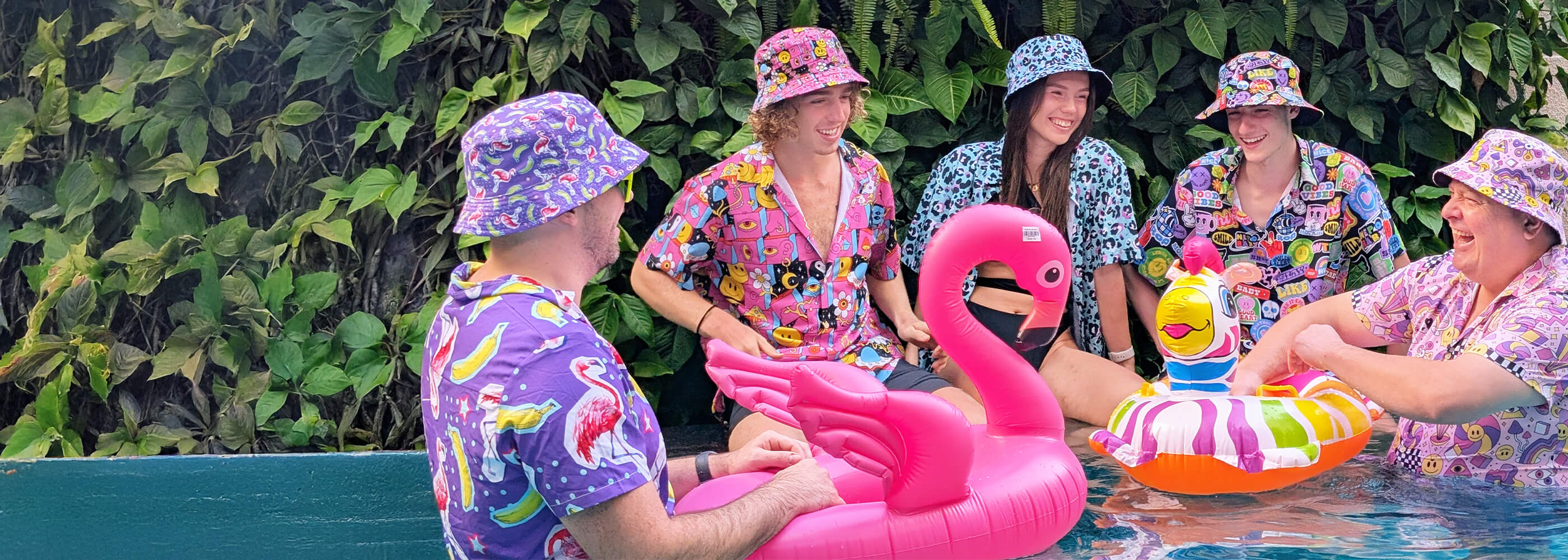People in colourful bucket hats, shit shirts and swimsuits with inflatable pool toys by a poolside.