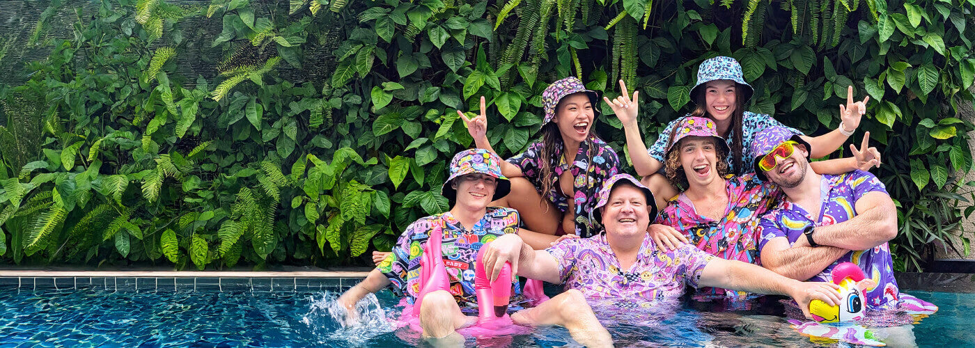 Group of people posing in a pool with colourful bad shirts and bucket hats.