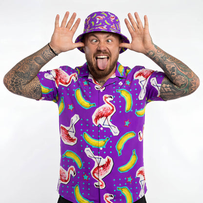 Man wearing a purple shirt with flamingo and banana pattern and matching bucket hat on a white background