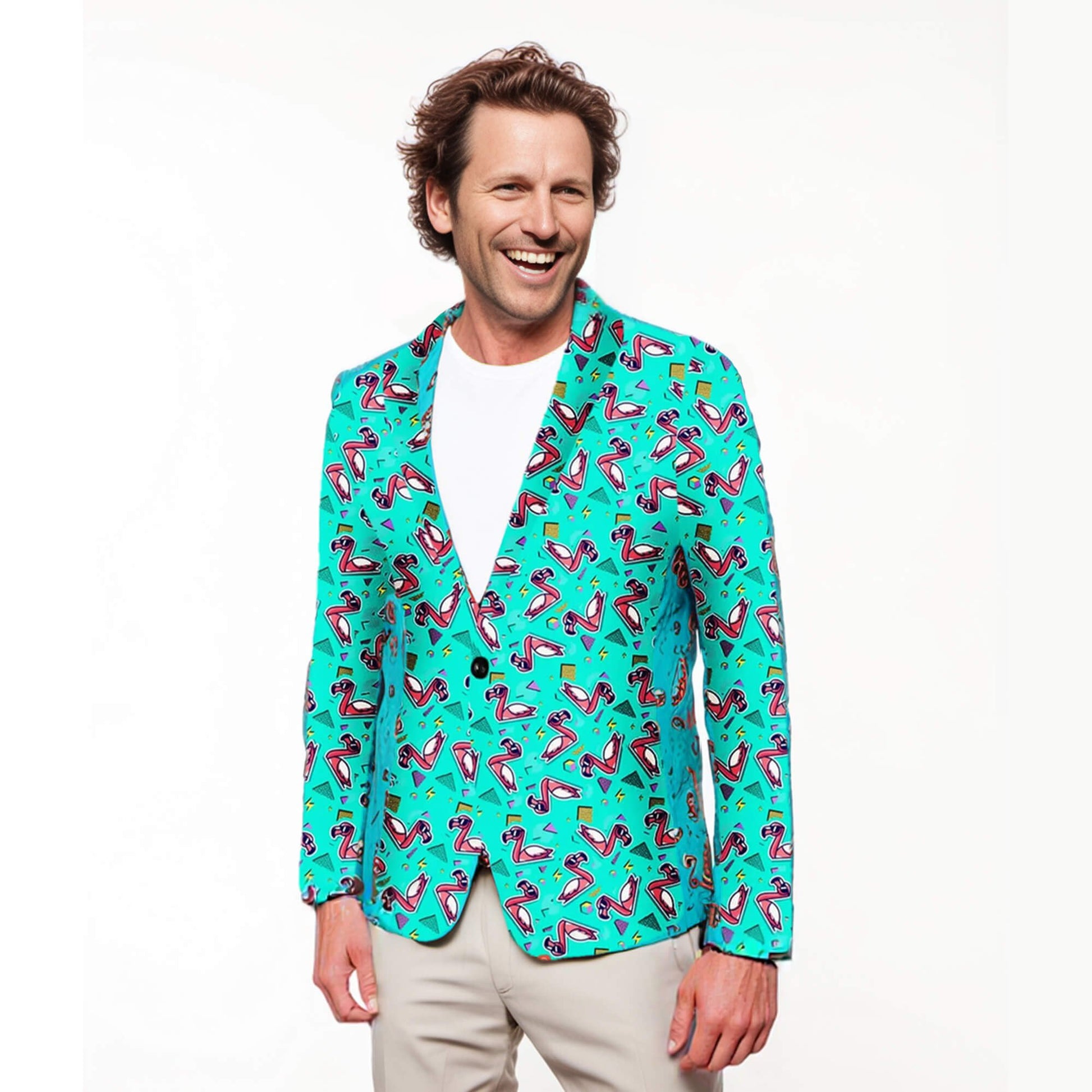 A man smiles in the Flamingo Fandango Blazer, featuring playful pink flamingos and geometric designs, styled over a white tee and beige pants against a plain white background.