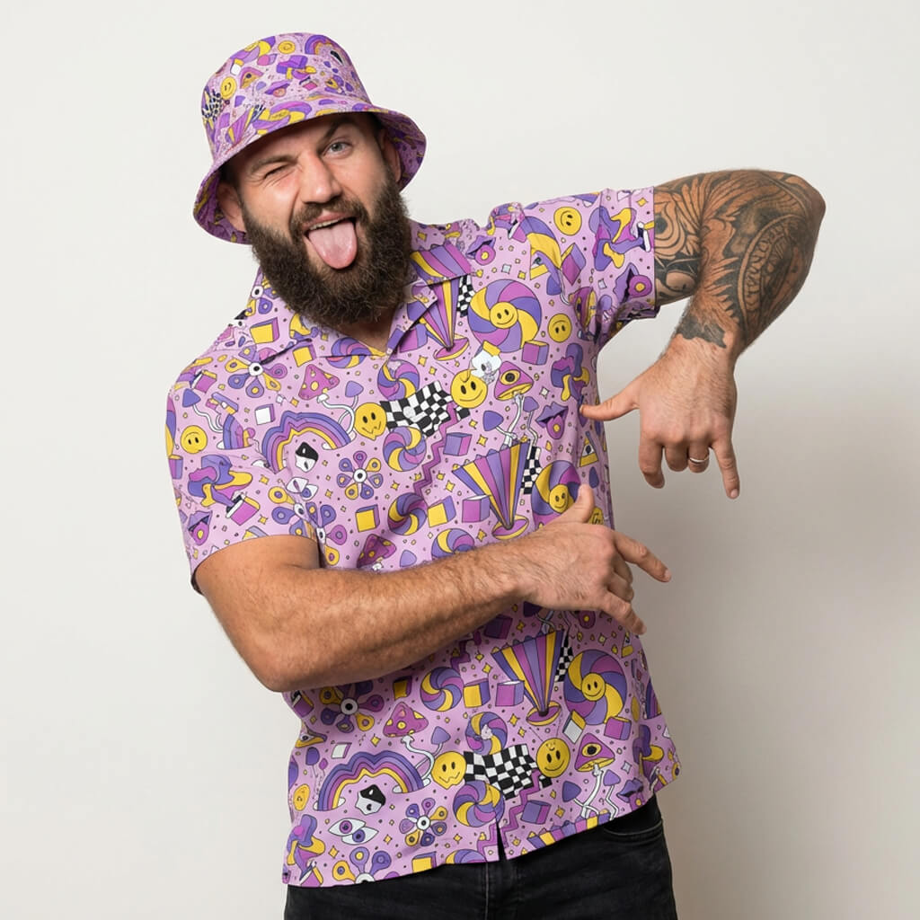 Man wearing a purple patterned shirt and bucket hat, pointing at himself against a white background