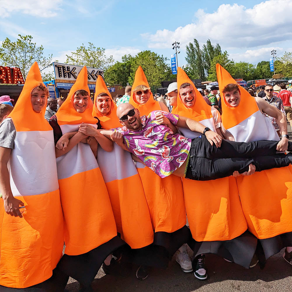 Seven people, six dressed in orange and white traffic cone costumes, pose together outdoors at an Twickenham for the Rugby Sevens. They are smiling, and the group is holding up a man wearing a colourful shit shirt and sunglasses.